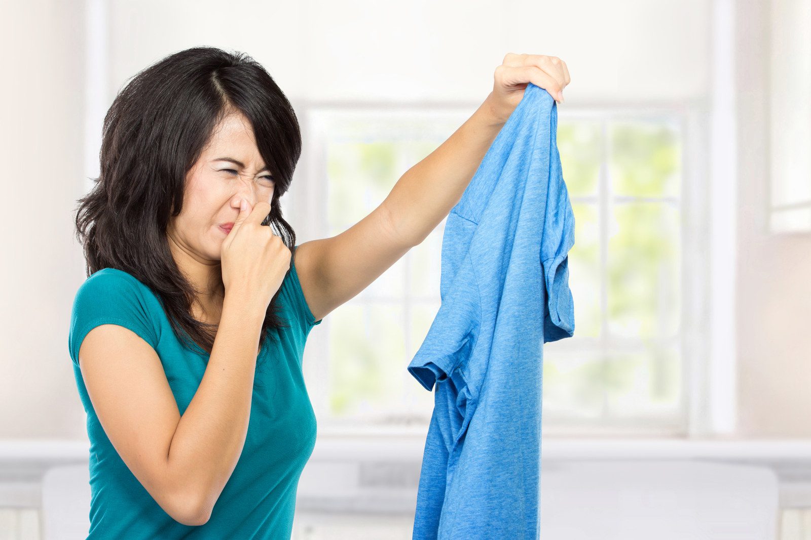 a woman covering her nose with hand and holding a smelly shirt in her second hand.