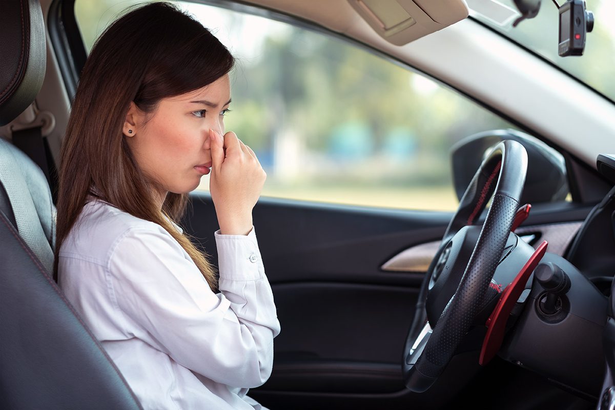 a woman pinching her nose because of the odor in her car.